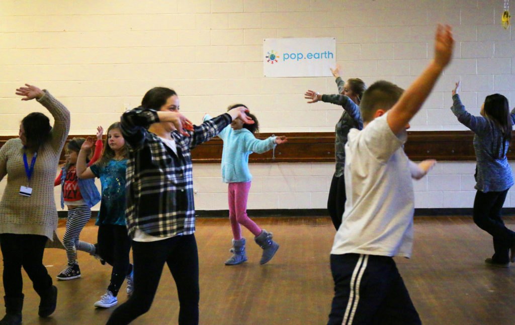 Children and teens dancing with arms raised in a You Can Dance class